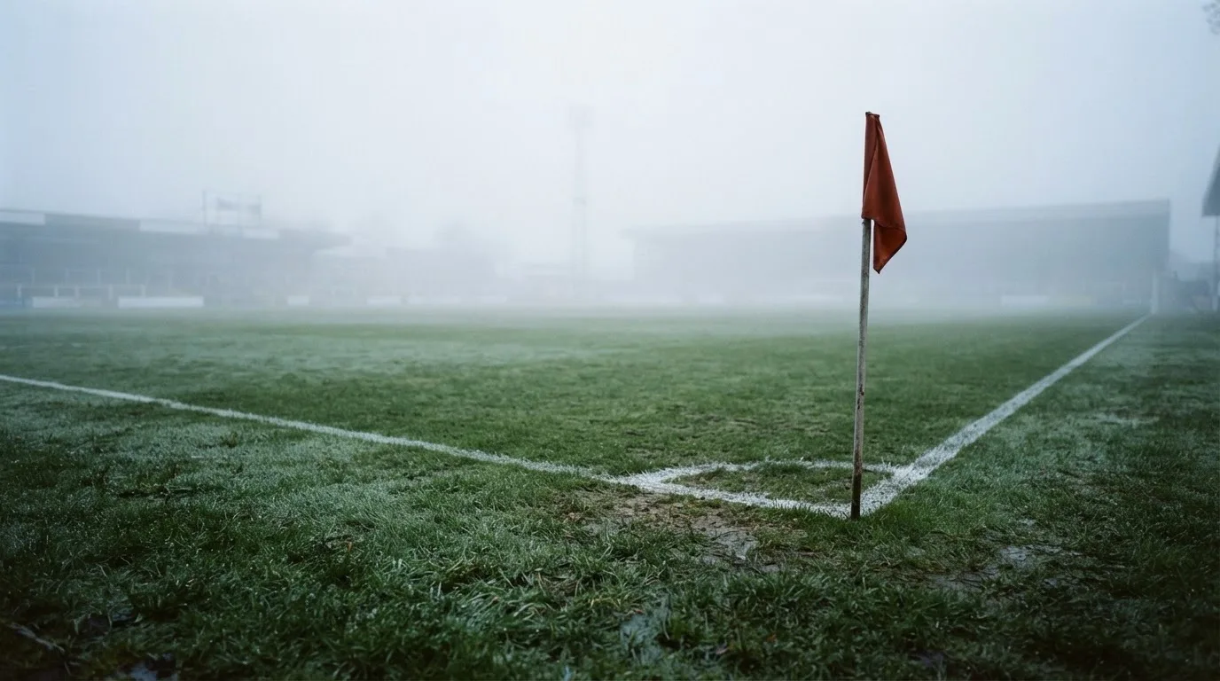 Der Rand eines Spielfelds mit weißer Linie und Eckfahne bei Nebel am frühen Morgen, ohne Menschen.