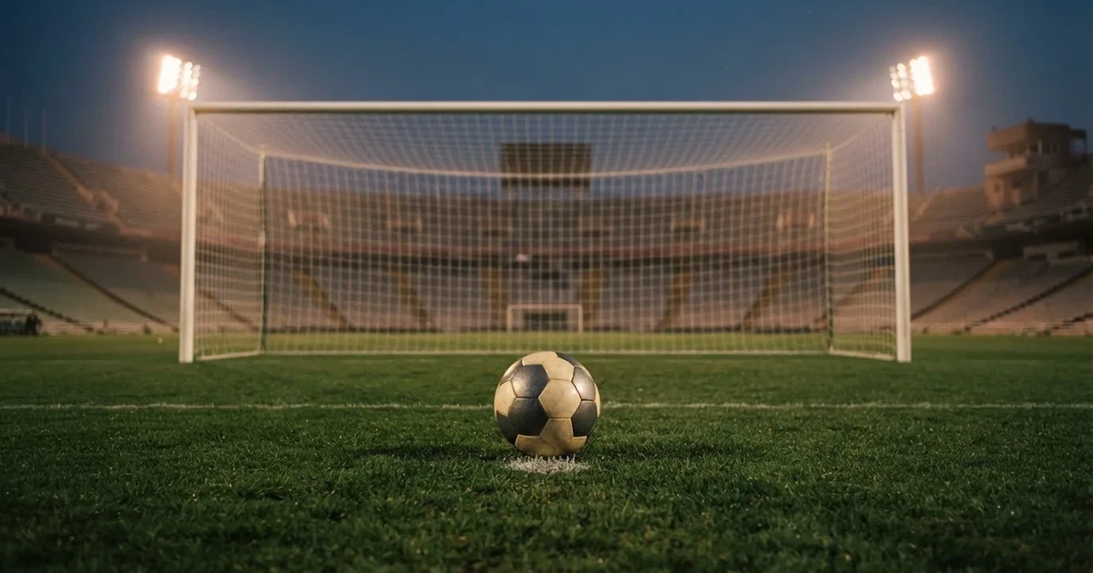 Ein Fußball liegt im Strafraum direkt vor dem Tor mit Netz, im Hintergrund leere Ränge bei Dämmerung.