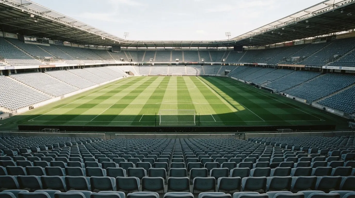 Ein leeres Fußballstadion bei Tageslicht von der Tribüne aus gesehen, der Rasen zeigt gleichmäßige Mähstreifen.