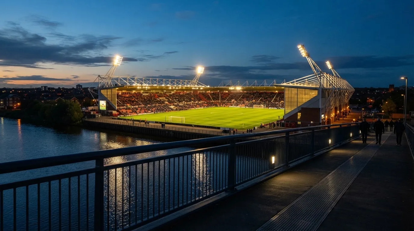 Ein Stadion bei Dämmerung mit eingeschalteten Flutlichtmasten, von einer Brücke aus aufgenommen.
