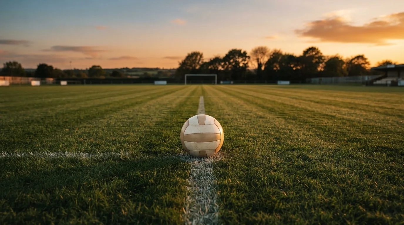 Ein Fußball liegt in der Mitte eines leeren Rasenplatzes, am Horizont färbt sich der Himmel orange.