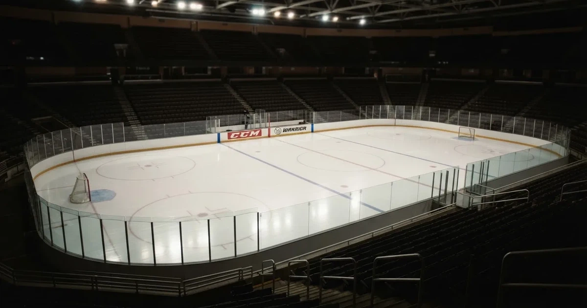 Eine Eishockeyhalle von der Tribüne aus gesehen, spiegelglatte Eisfläche, Banden ohne Schriftzüge, helles Flutlicht.