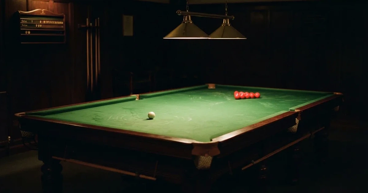 Ein Snookertisch mit grünem Tuch und aufgebauten roten Kugeln in einem abgedunkelten Raum unter einer hängenden Lampe.