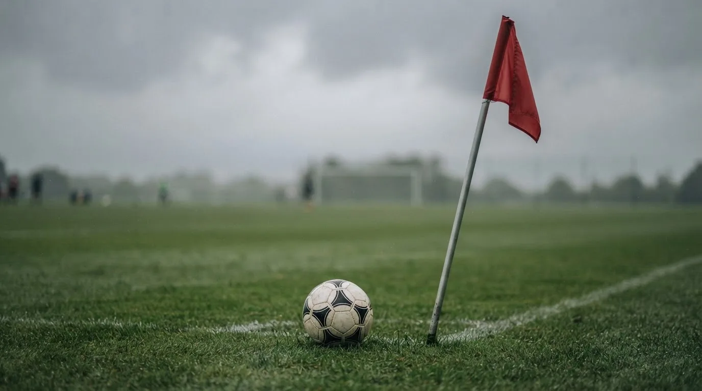 Ein Fußball liegt neben einer Eckfahne auf kurz gemähtem Rasen unter bewölktem Himmel.